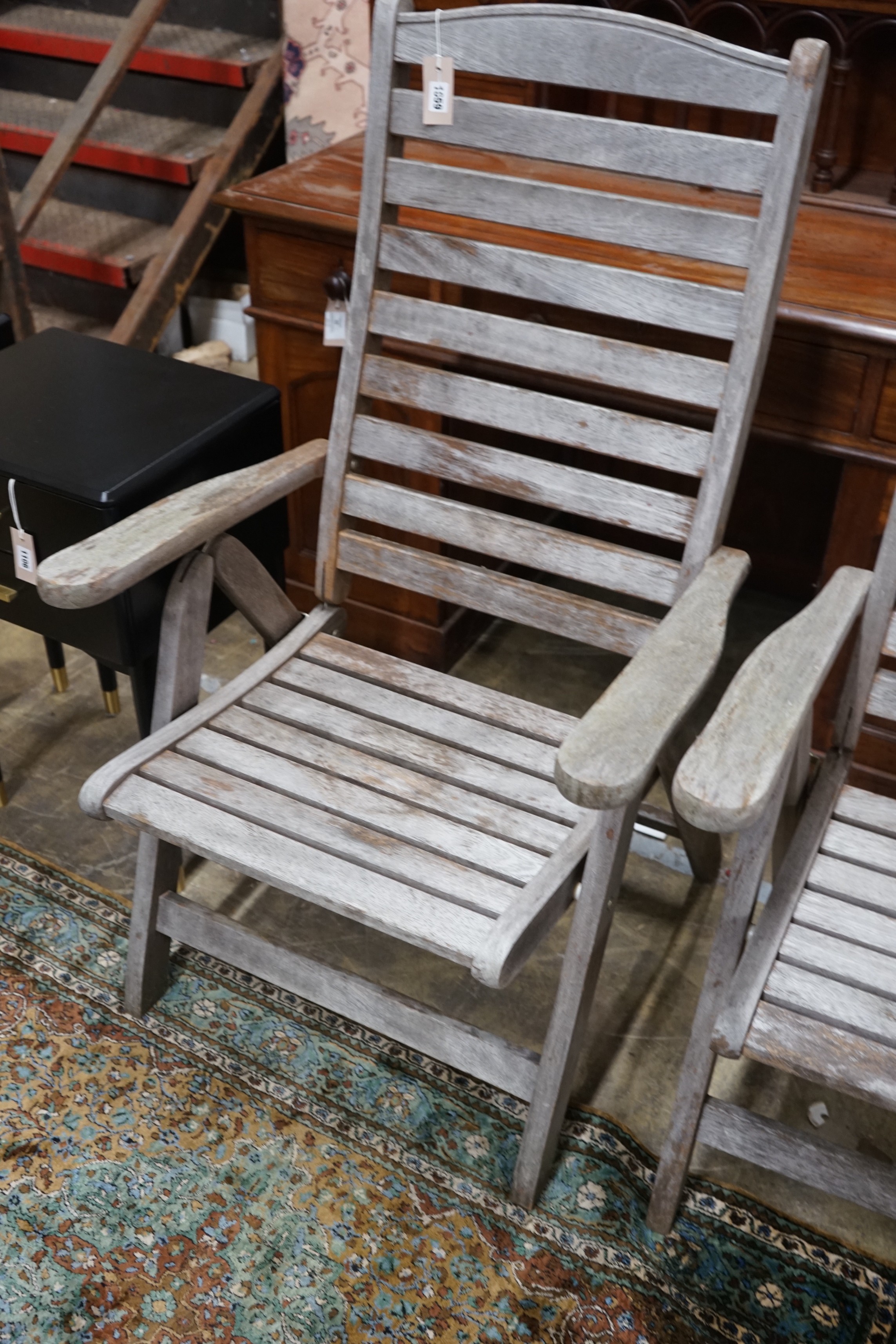 A pair of weathered teak folding garden armchairs, height 112cm